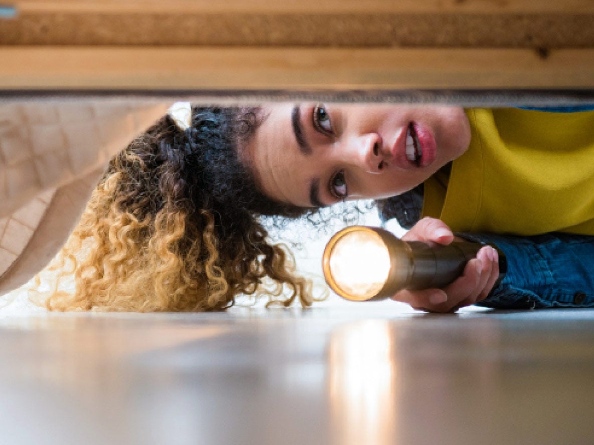 Woman looking under bed with torch